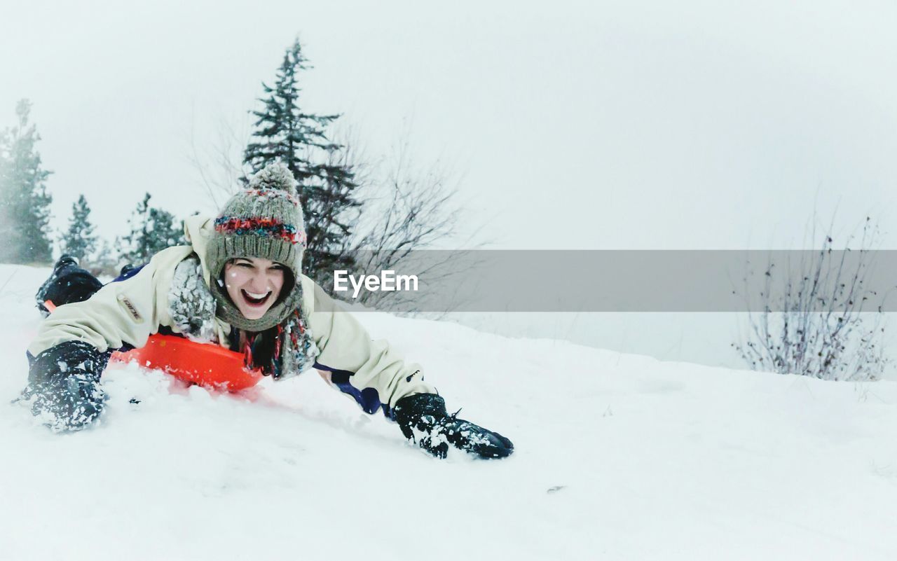 Happy young woman sledding on snowcapped mountain during winter