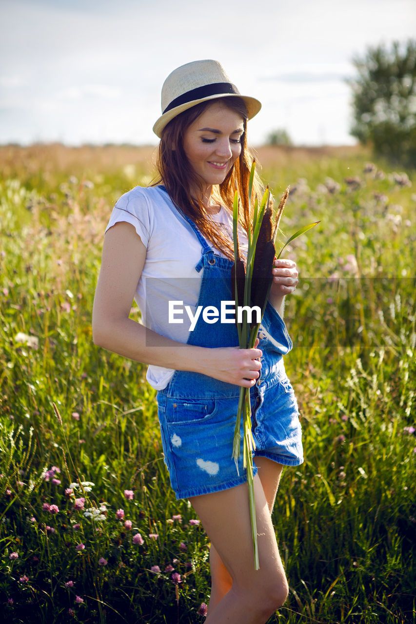 Portrait of young girl in overalls and a hat, standing with cane in hand in field