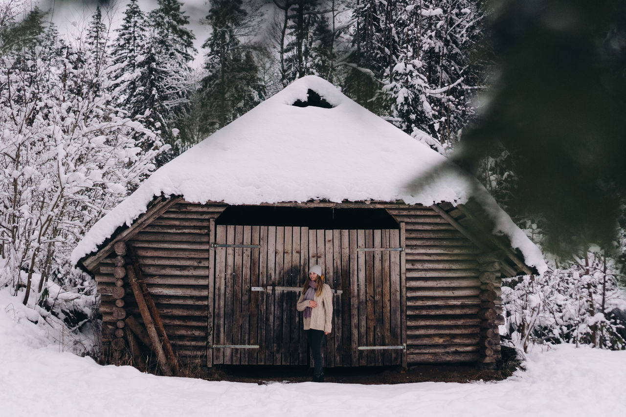 Woman standing on snow covered land against trees and buildings