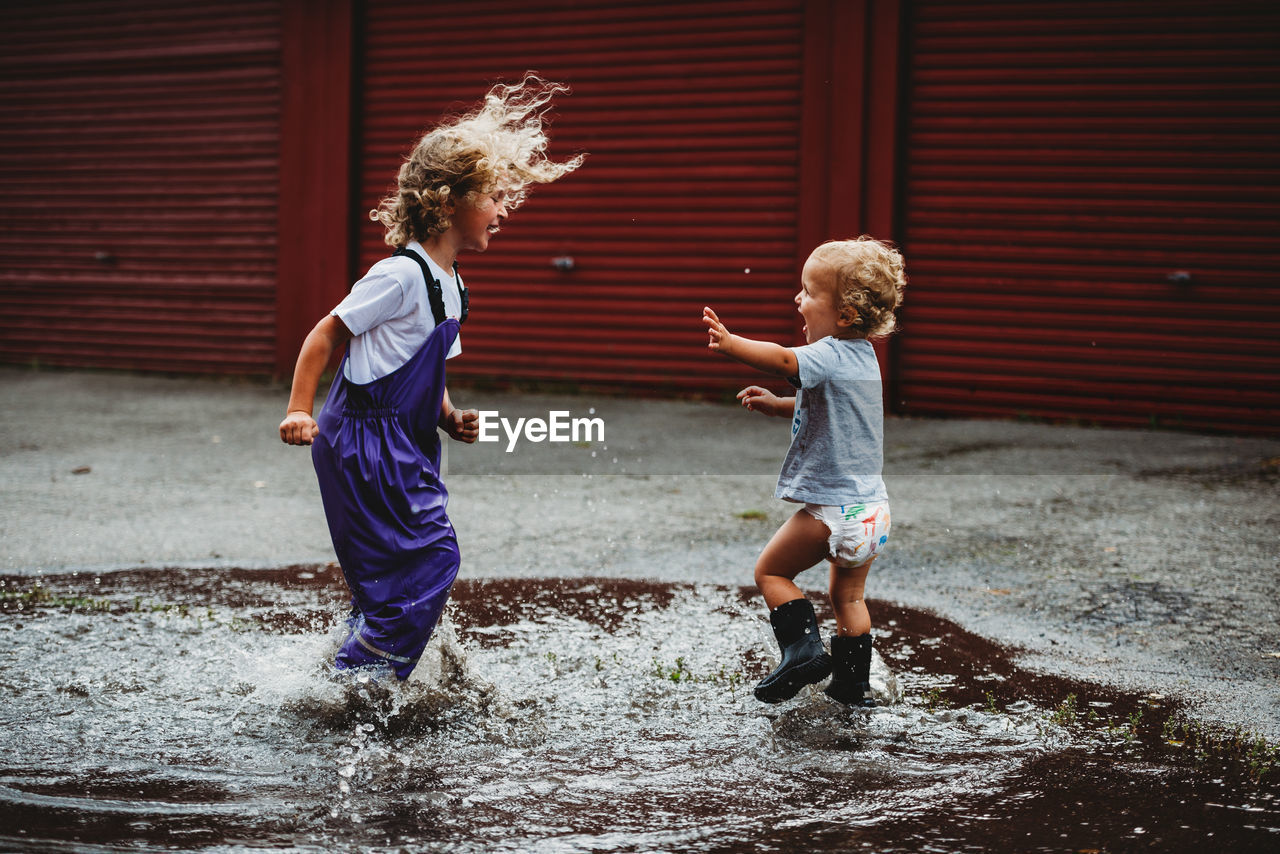 Siblings boy and girl jumping in a puddle having fun