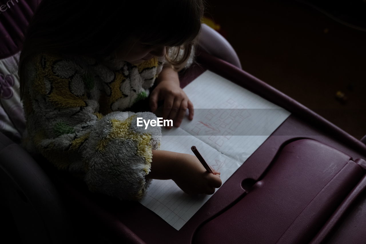 High angle view of girl writing on book at home