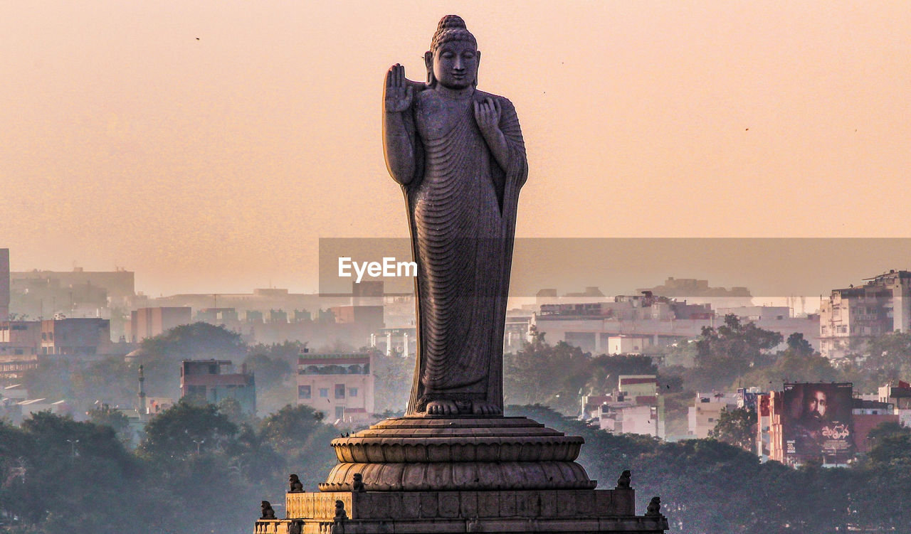 Buddha statue in city against clear sky during sunset
