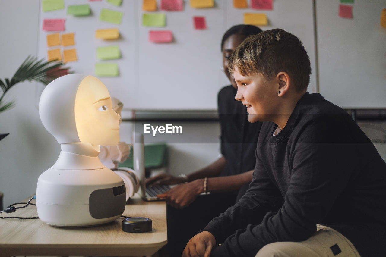 Smiling boy communicating with illuminated ai robot in innovation lab