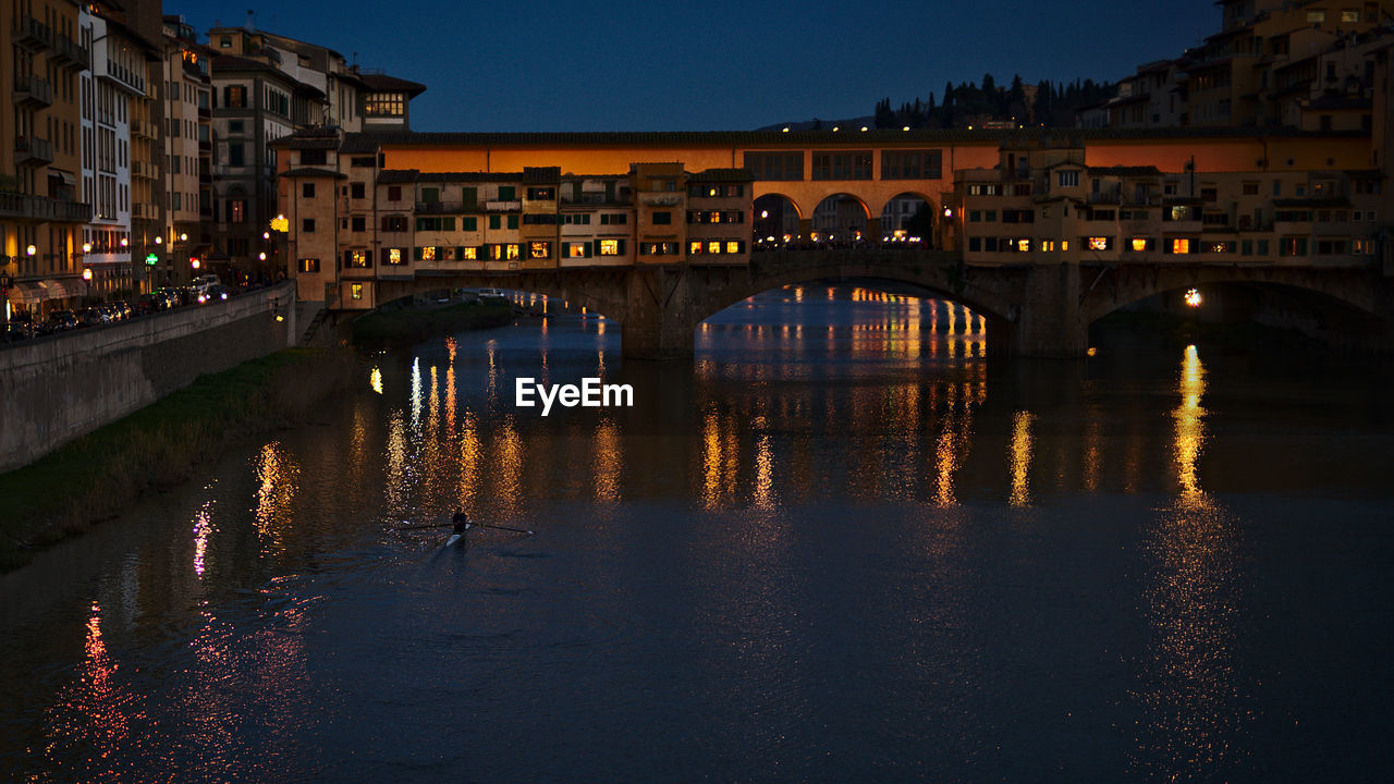 ILLUMINATED BRIDGE OVER RIVER BY BUILDINGS AGAINST SKY