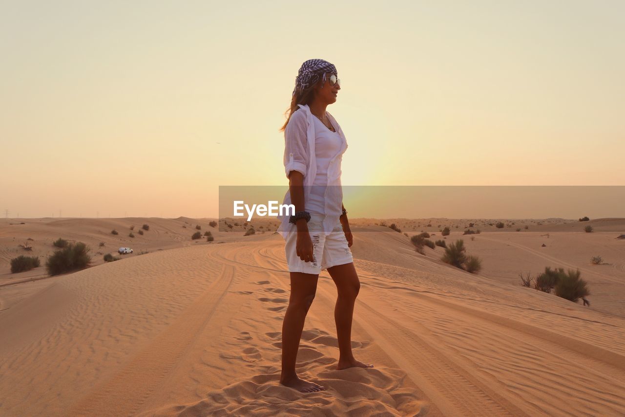 Full length of woman standing on sand against clear sky during sunset