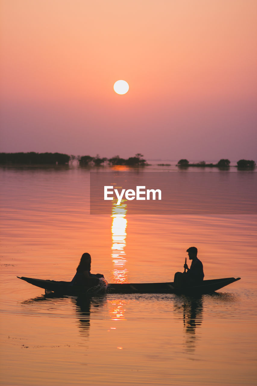 Silhouette people in boat against clear sky during sunset