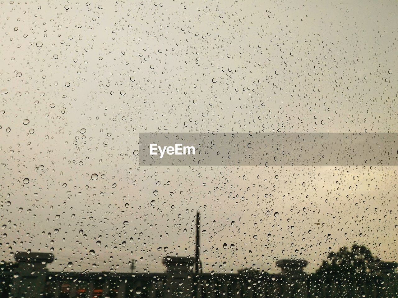 Buildings against sky seen through wet glass window