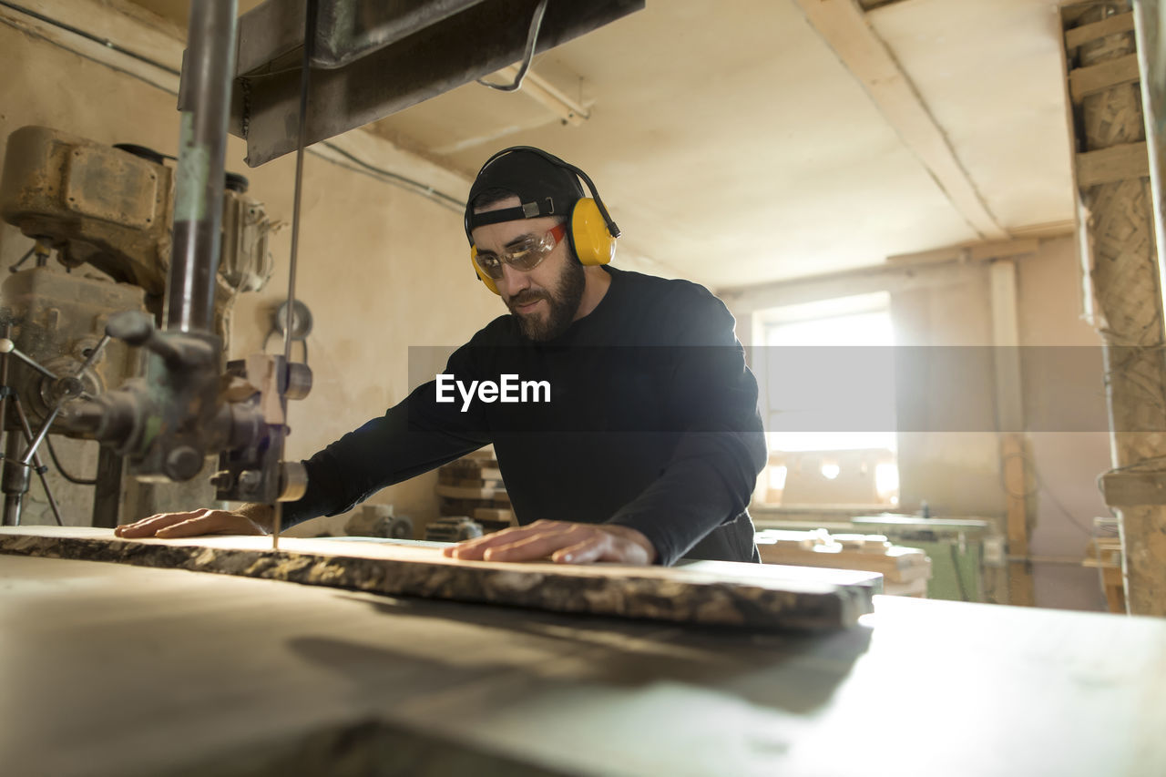 Woodworker sawing wood through bandsaw in workshop