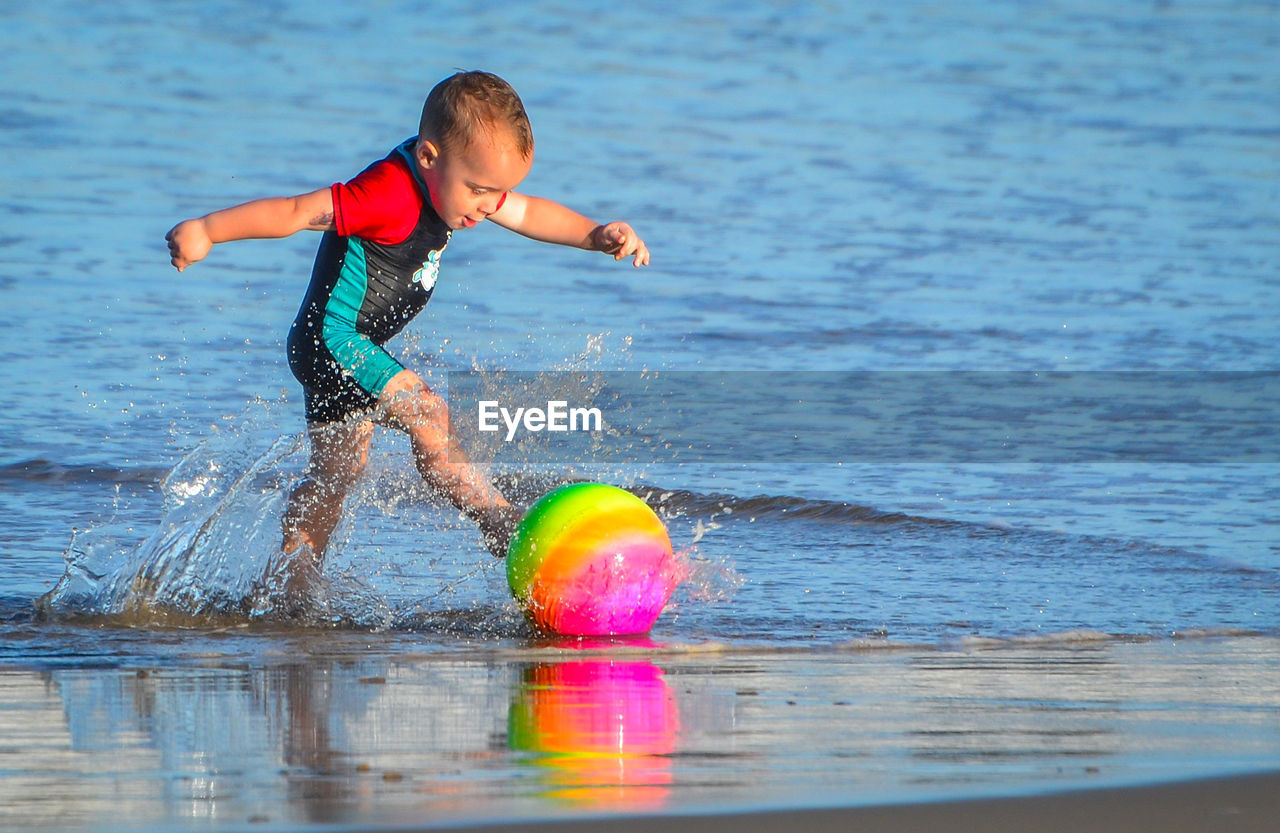 Boy kicking ball on shore at beach