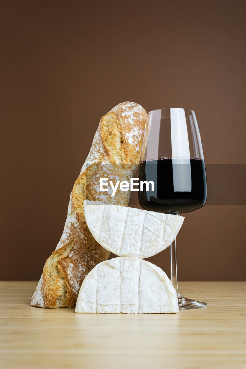 Minimalistic composition of a glass of red wine, a baguette, and camembert cheese.