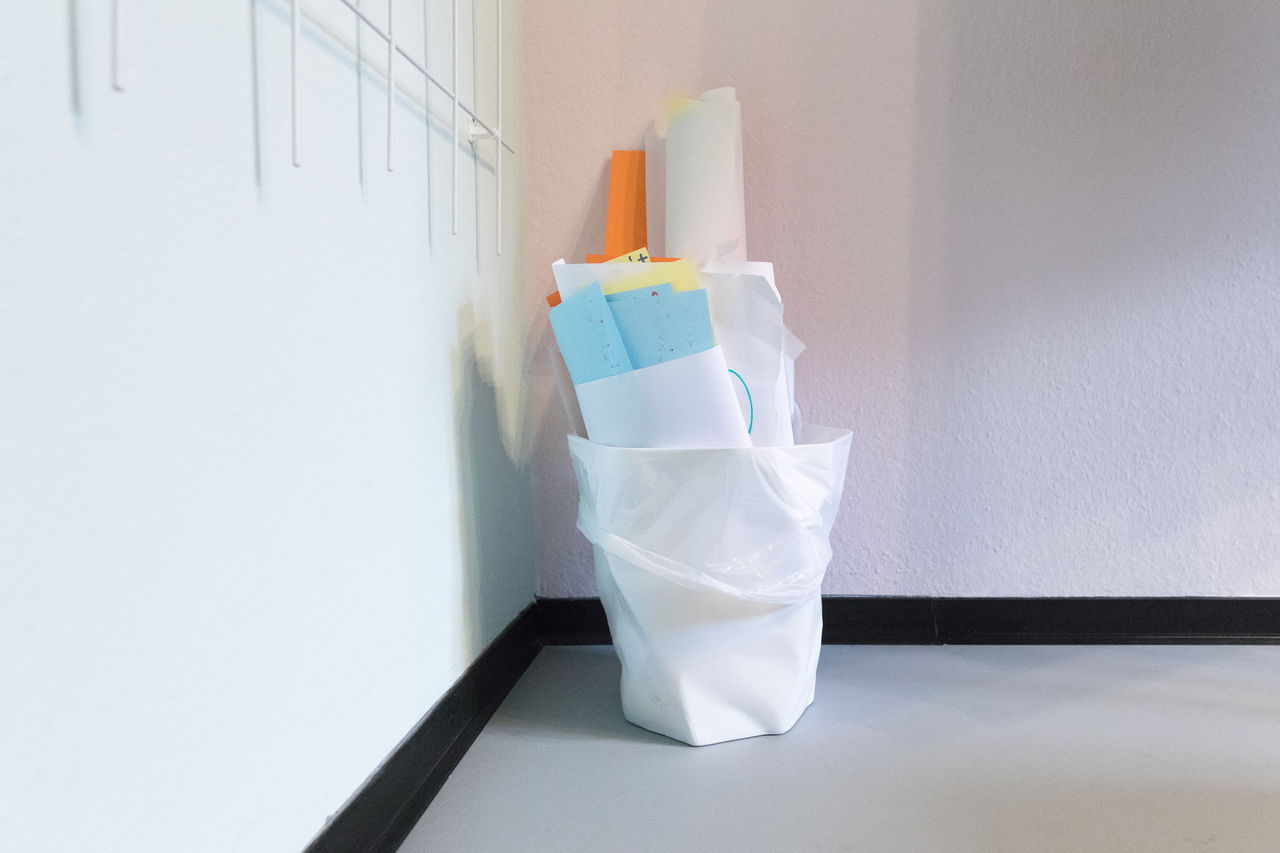 Close-up of papers in dustbin on floor against wall at home