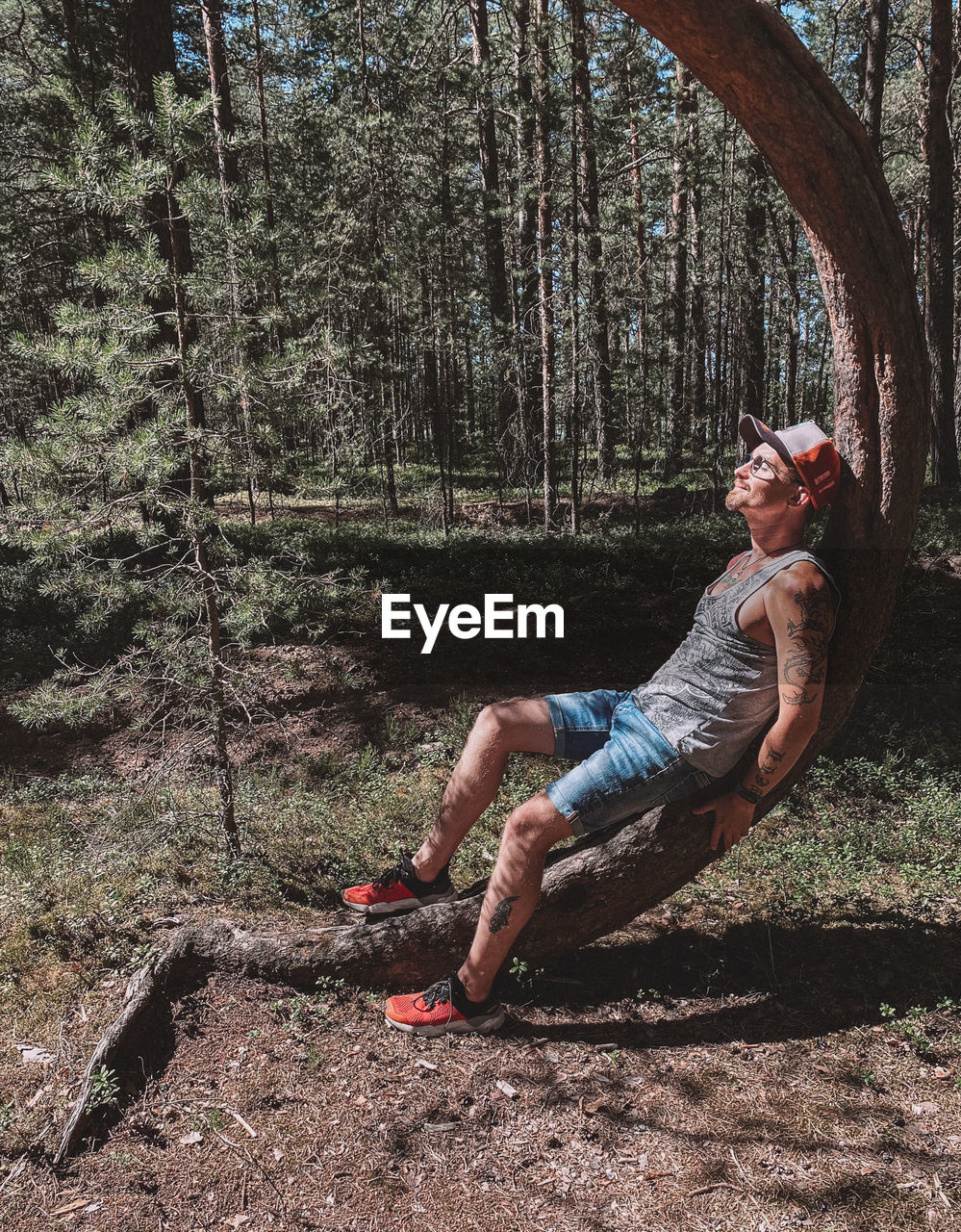 Side view of man sitting on tree trunk in forest