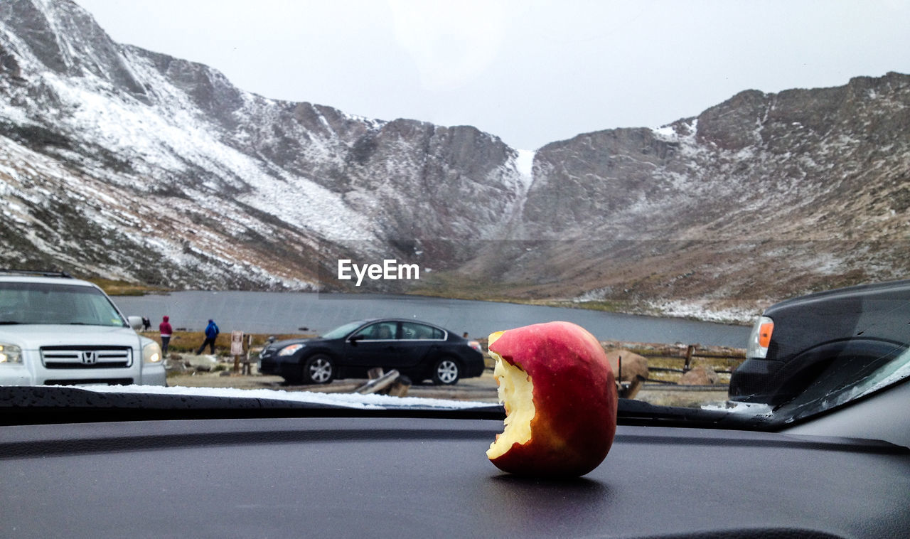 Close-up of eaten apple on dashboard against lake by mountains during winter