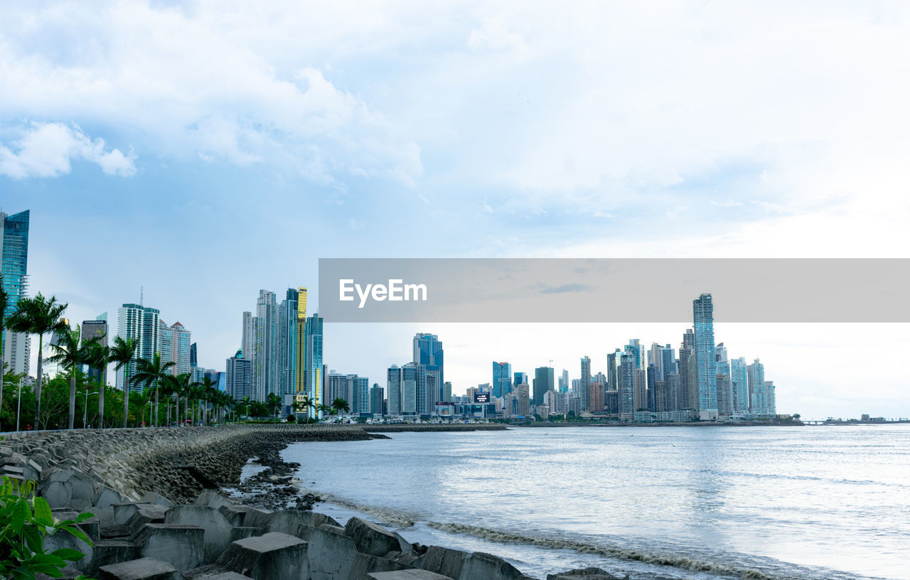 Sea by modern buildings against sky in city