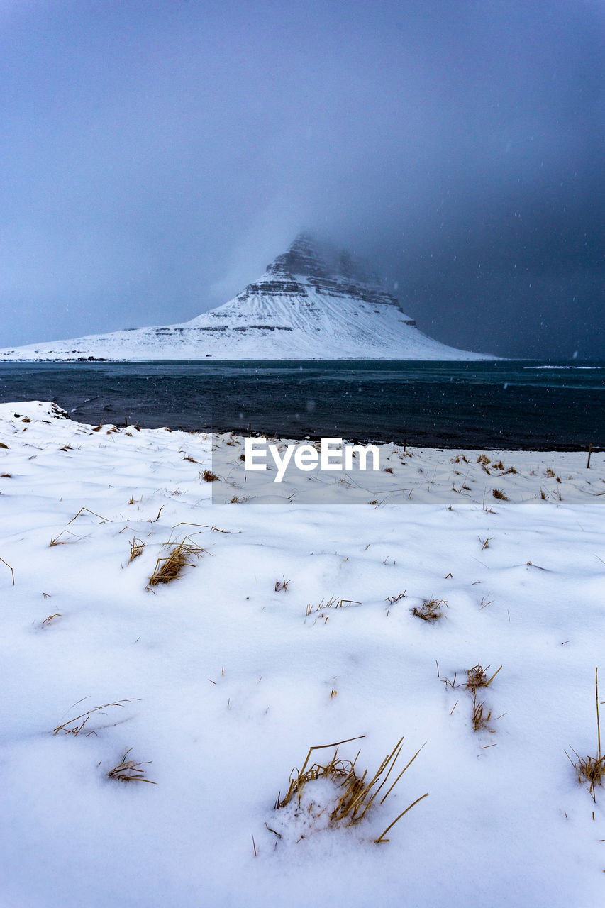 Scenic view of snow covered kirkjufell during a winter storm with snowflakes falling