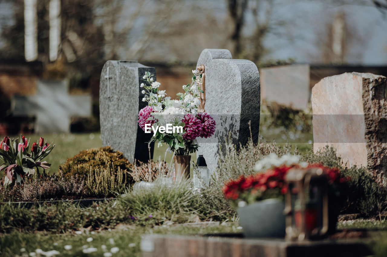 Grave stone with flowers at graveyard on sunny day with bouquet arranged on ground 