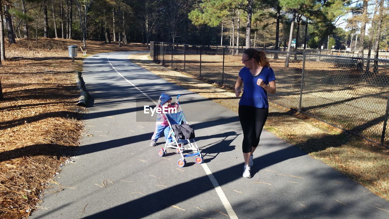 Full length of mother looking at child pushing baby stroller on road