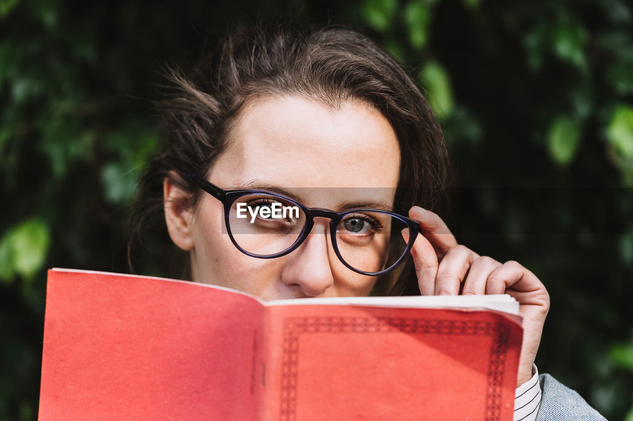 Content female student in glasses and with notepad standing in park and looking at camera