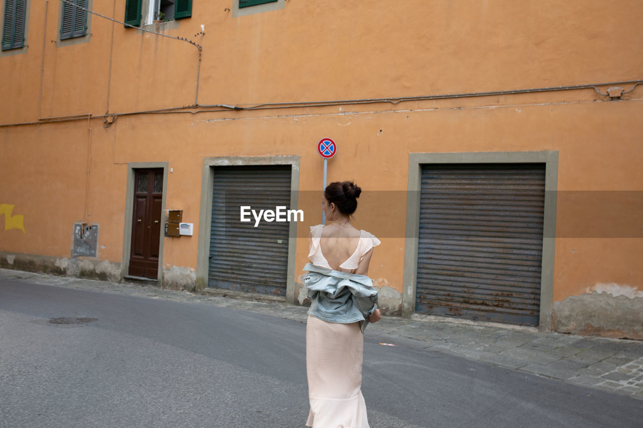 Rear view of woman standing on footpath against building