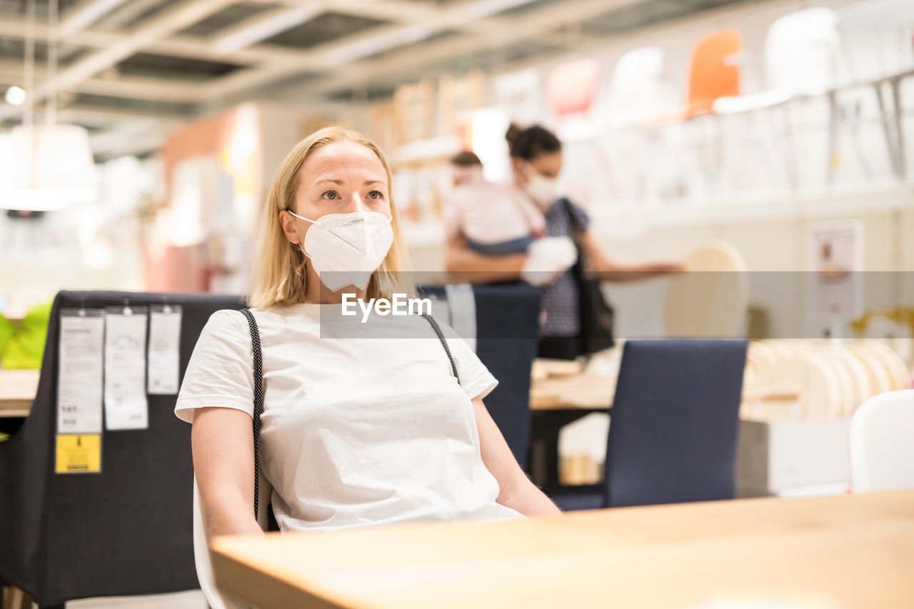 Close-up of woman wearing mask sitting at store