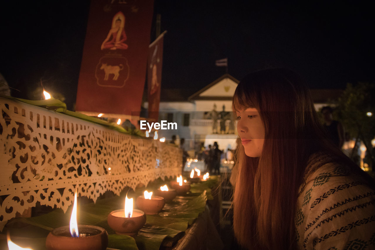 Woman looking at lit diyas at night