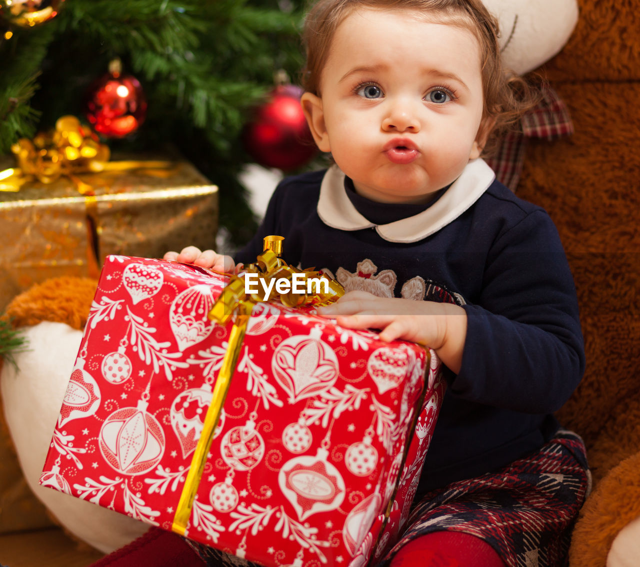 Cute girl with stuffed toy and gifts against christmas tree at home