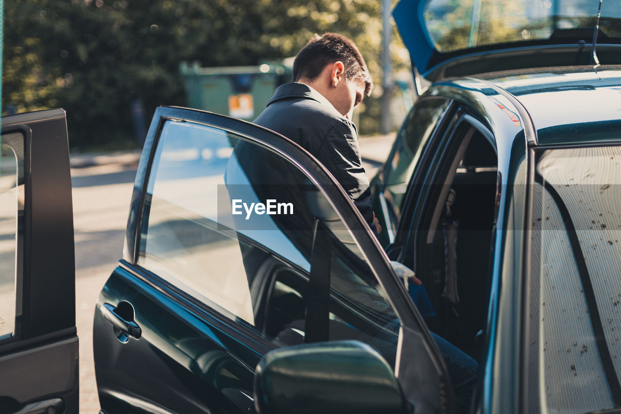 A young man stands near an open car door.