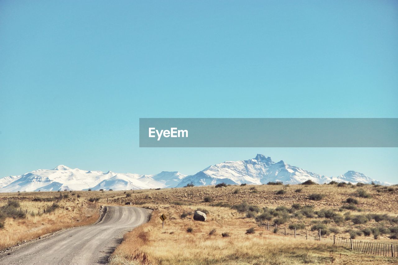 Road leading towards mountains against clear blue sky