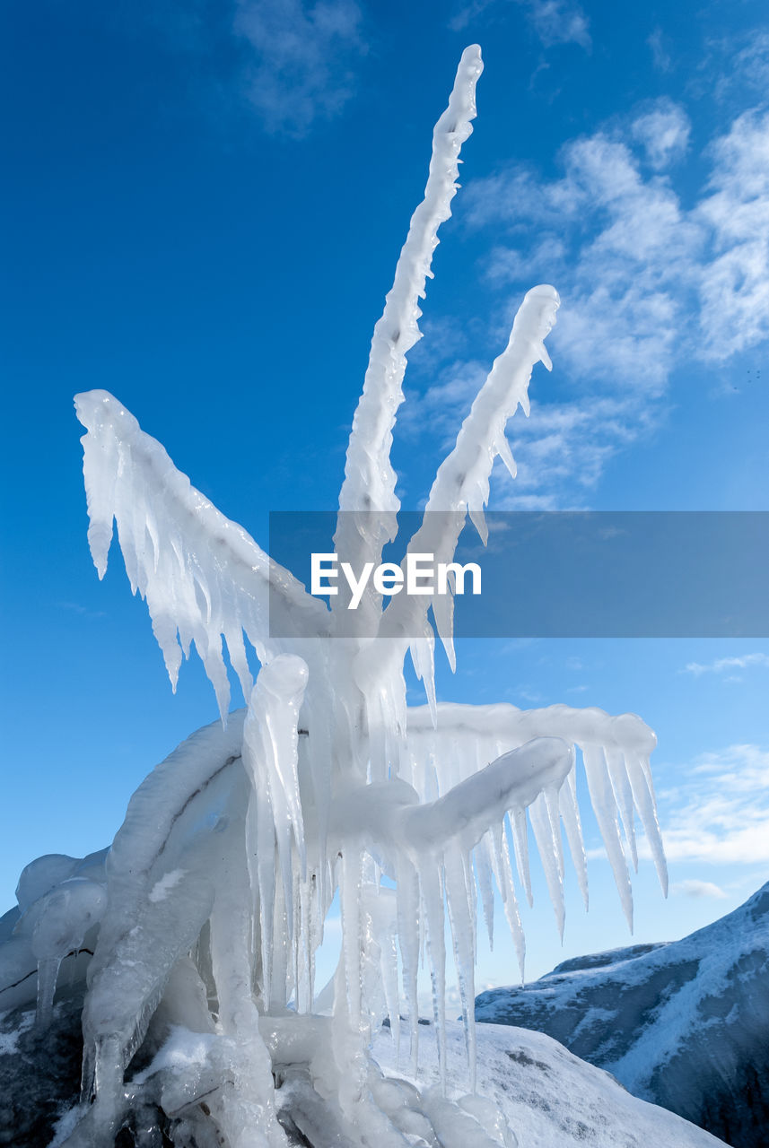 Icicles on snow covered landscape against blue sky