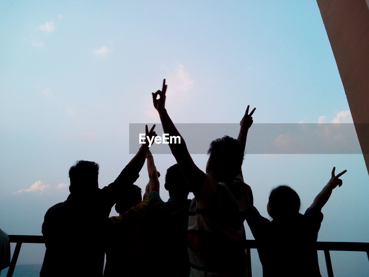 People gesturing peace sign against sky