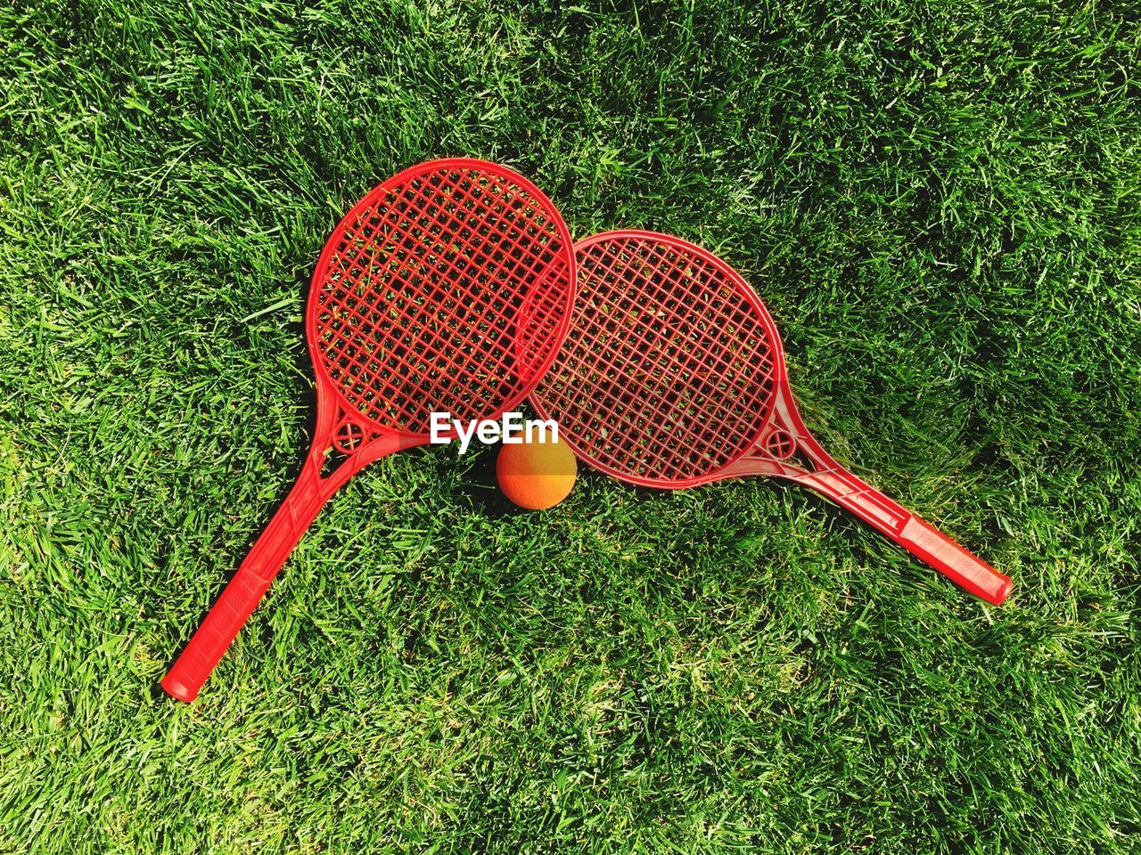 Directly above shot of red tennis rackets by ball on court