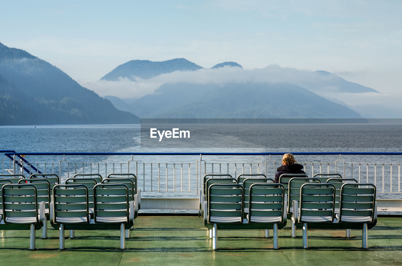 Rear view of woman sitting on chair at ship against mountains