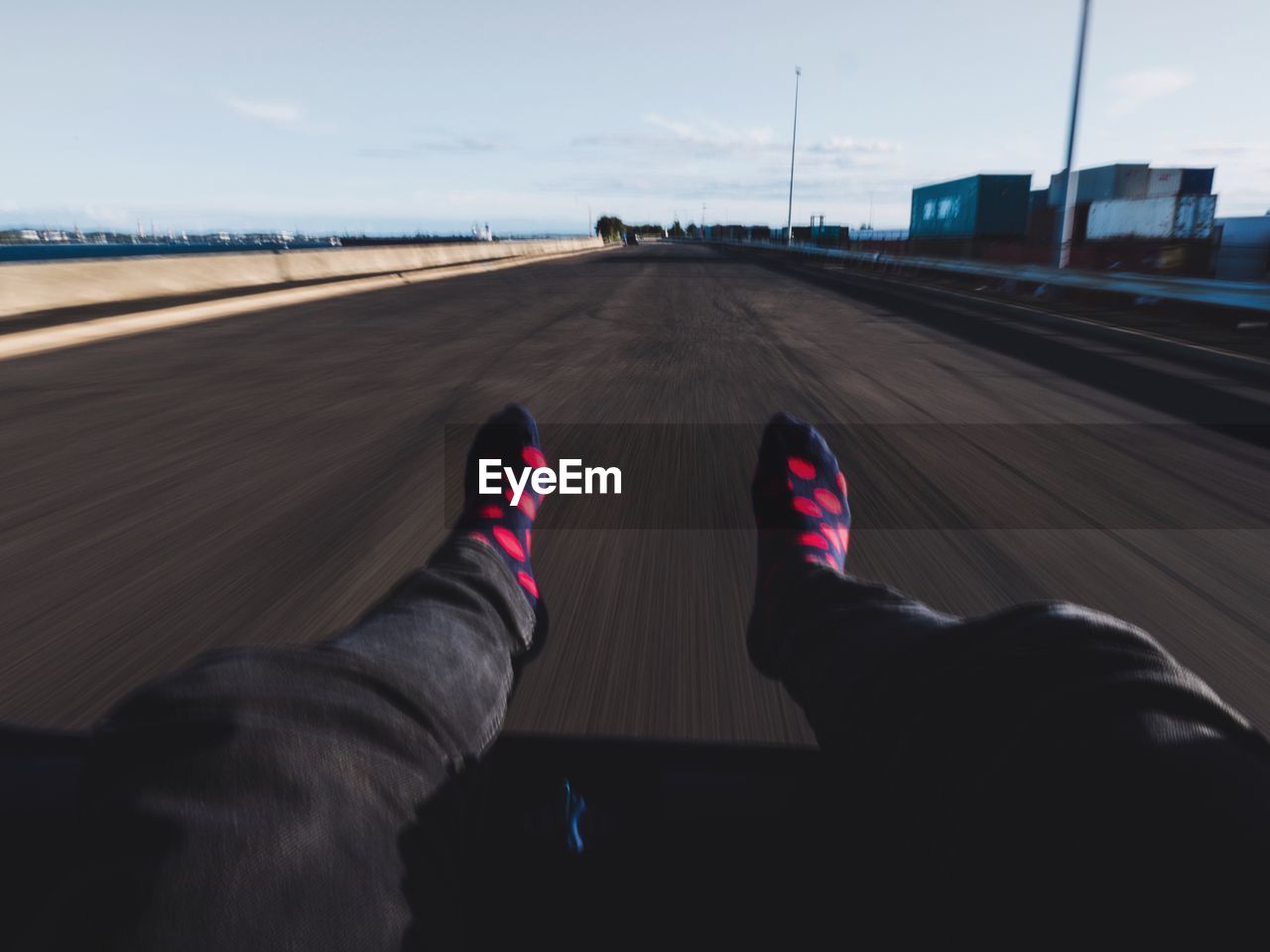 Low section of person relaxing in moving car against sky on road