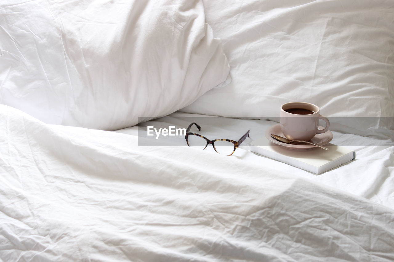 Elevated view of coffee cup and eyeglasses on bed
