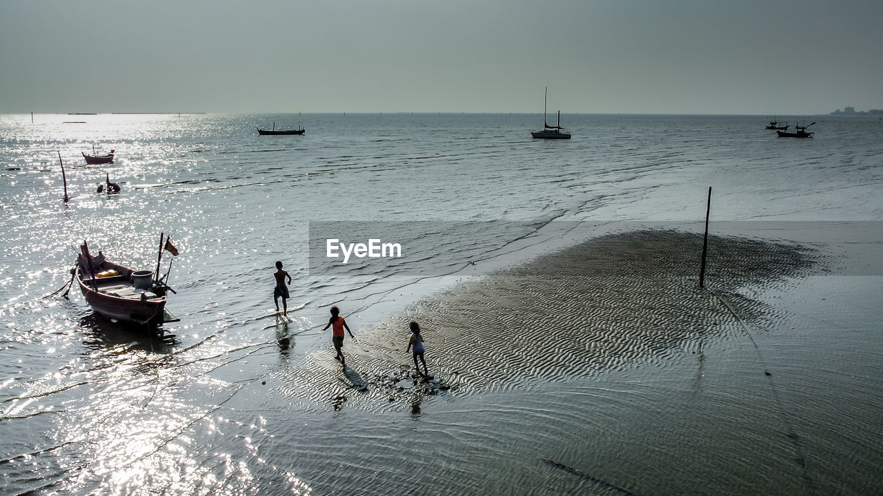 High angle view of children walking towards boats at beach