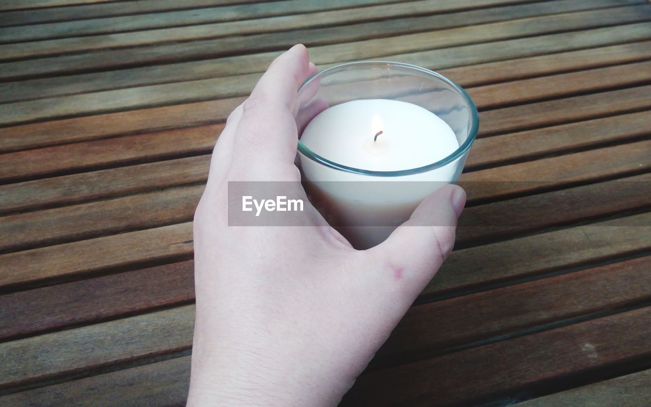 CLOSE-UP OF HAND HOLDING CUP OF GLASS OF WOODEN TABLE