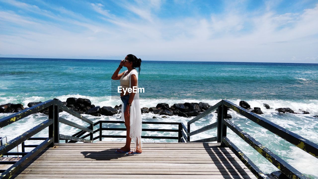 Young woman standing on a dock against blue sea and sky