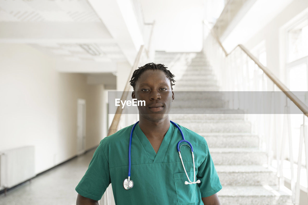 Confident doctor with stethoscope in front of steps at hospital corridor