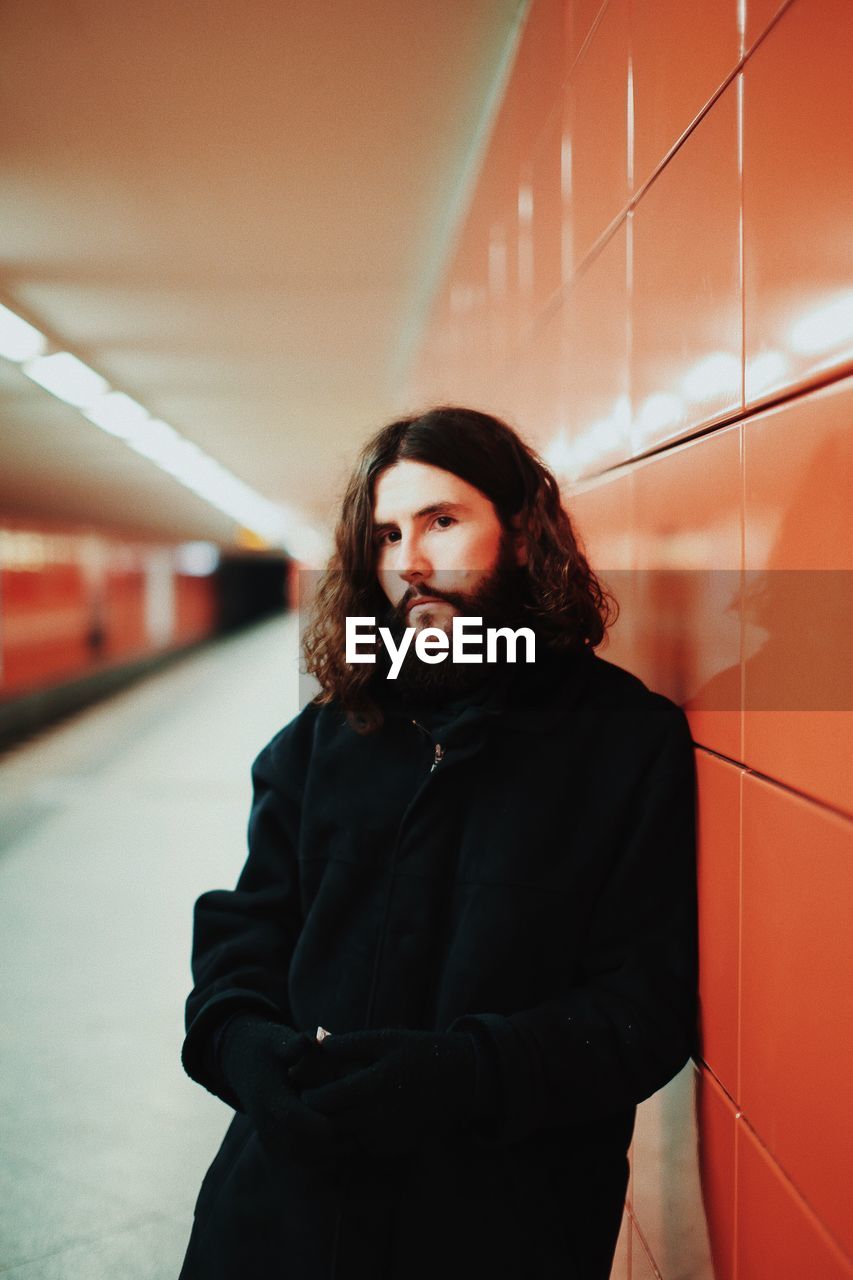 Young man looking away while standing by wall in subway station