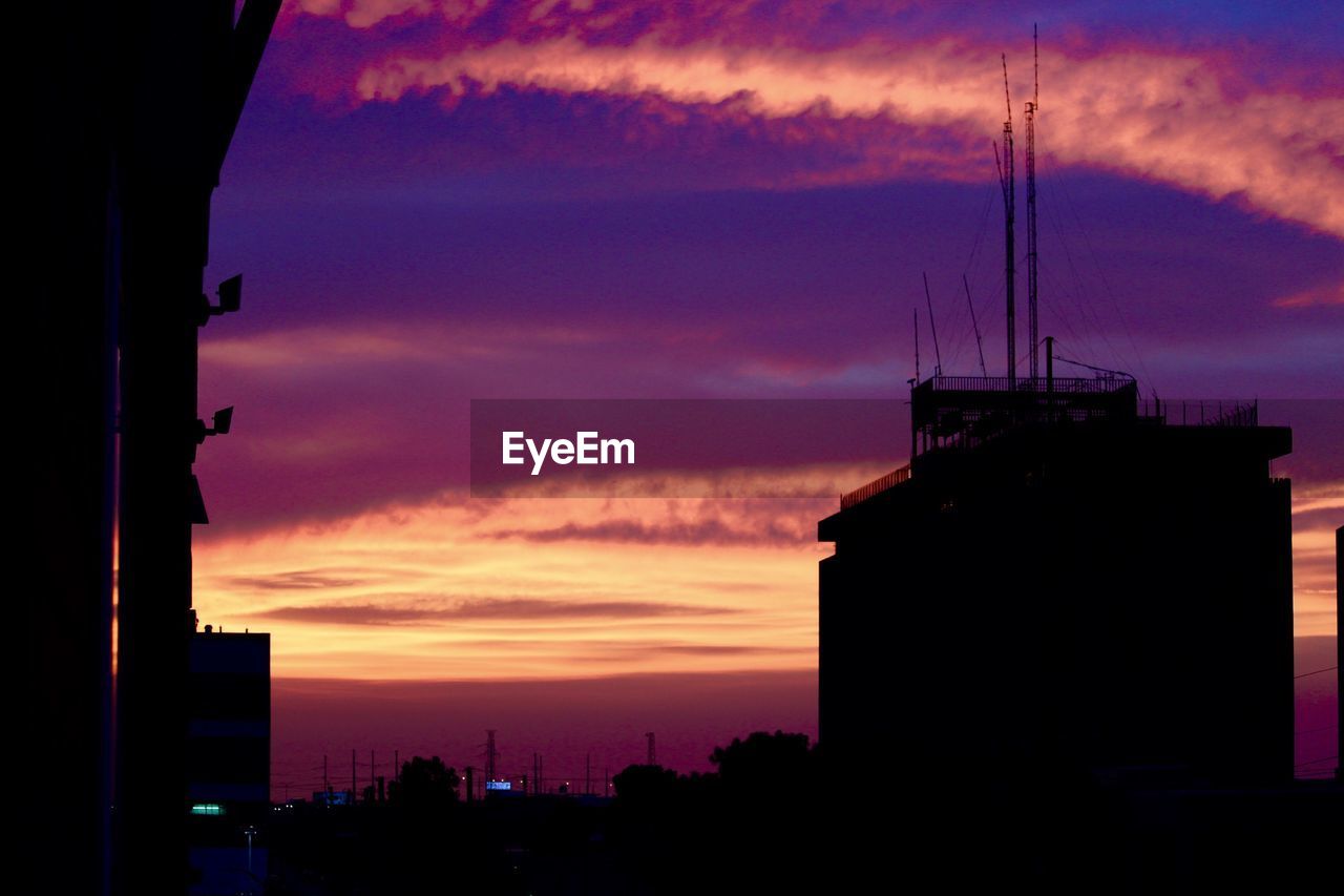 Silhouette buildings against cloudy sky during sunset