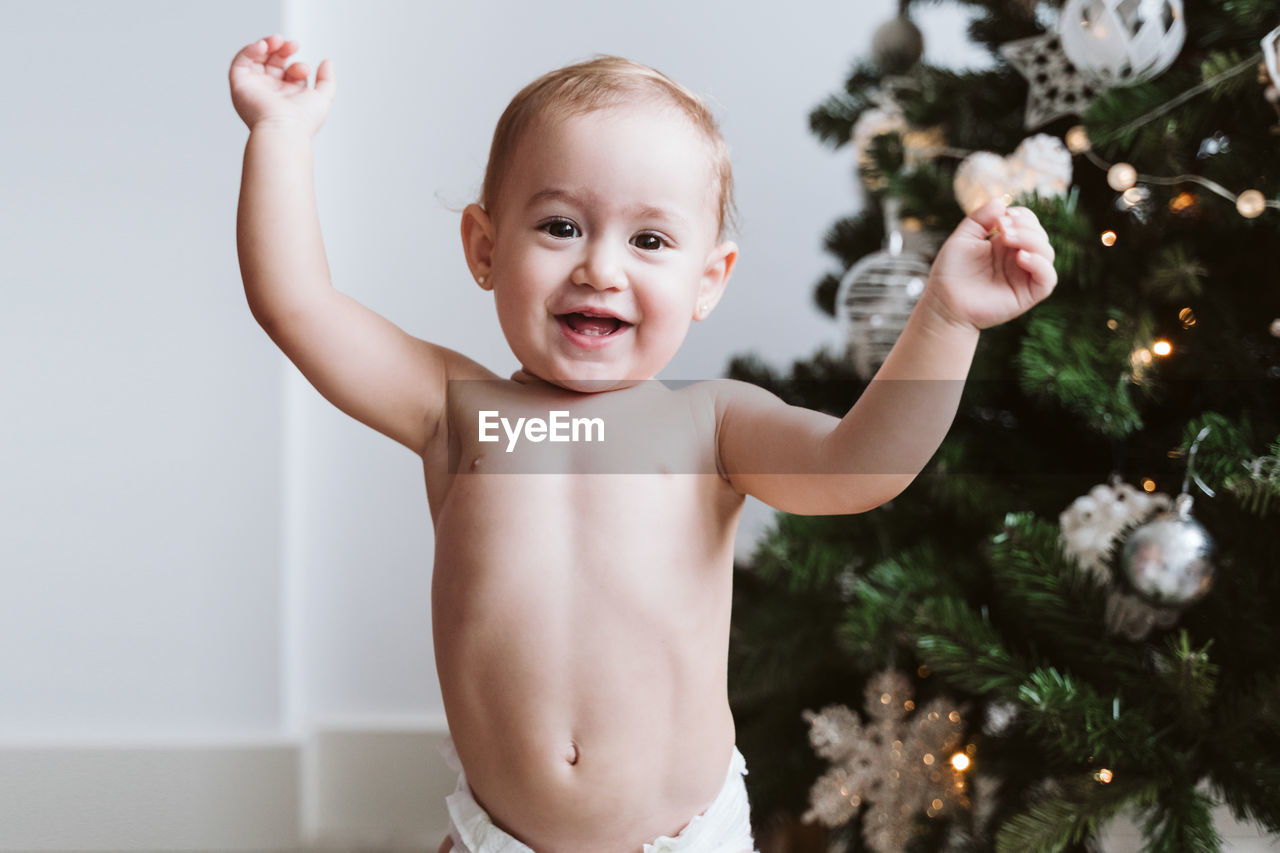 Happy baby girl wearing diaper decorating christmas tree