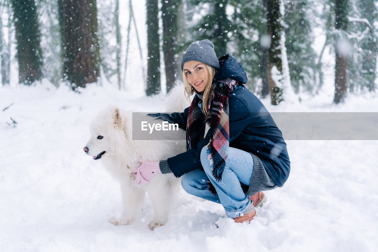 A young woman walks a dog in the park on a winter snowy day.