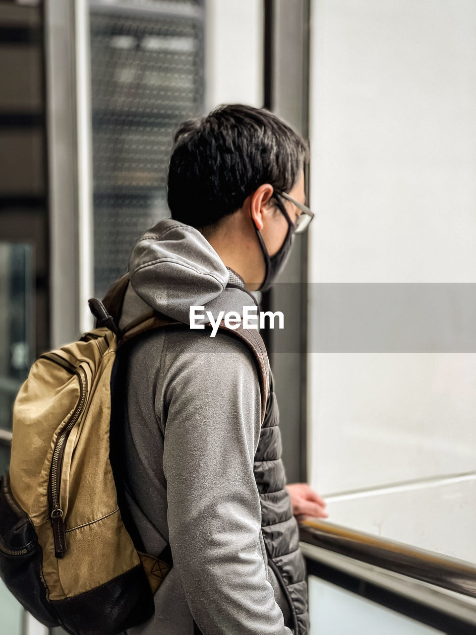 Rear view of man standing at railings and looking out of window.