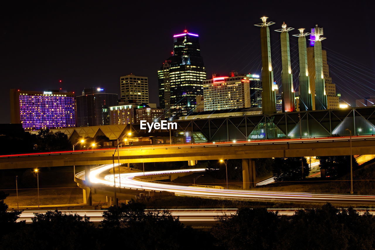 Illuminated buildings and bridge in city against sky