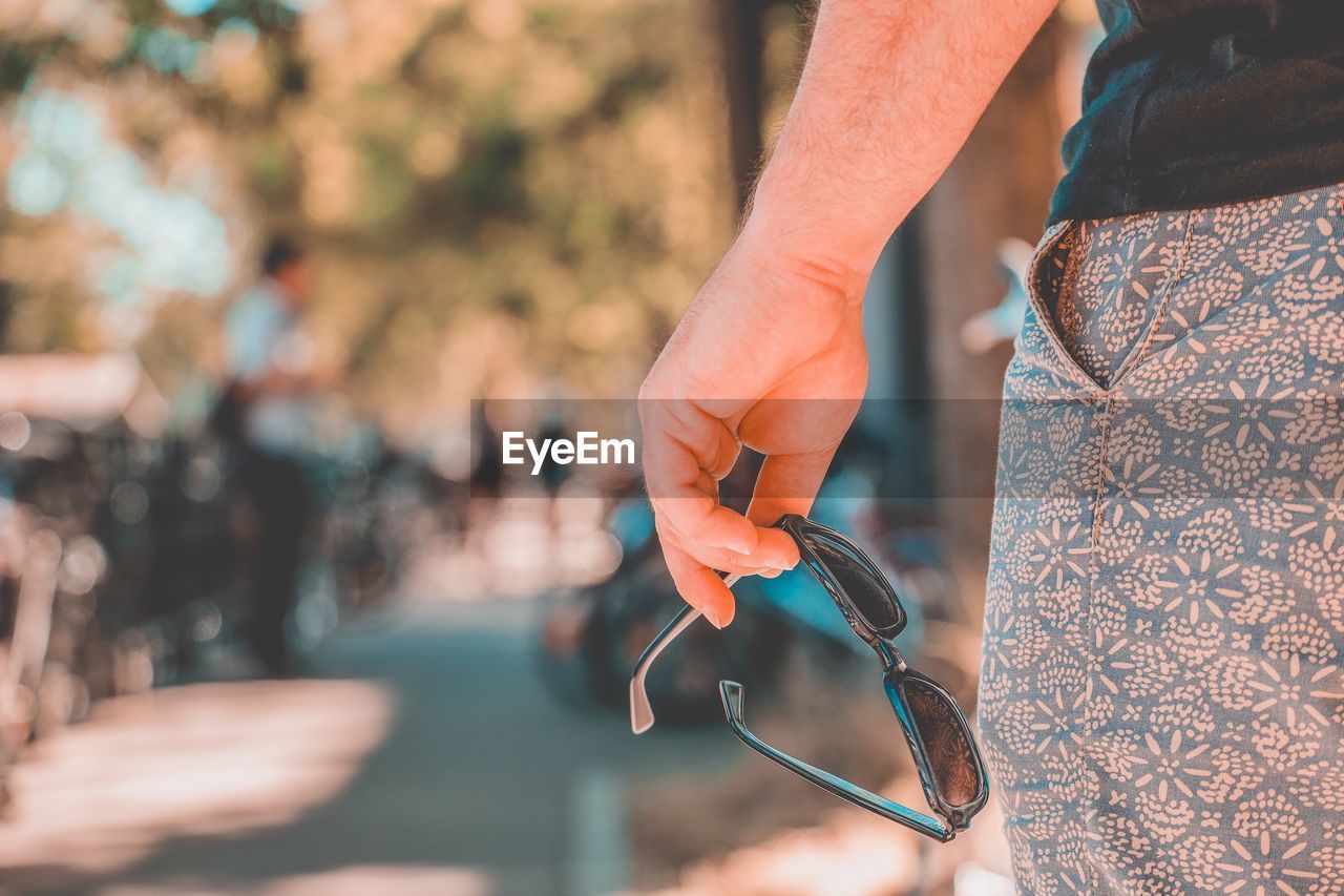 Midsection of man holding sunglasses