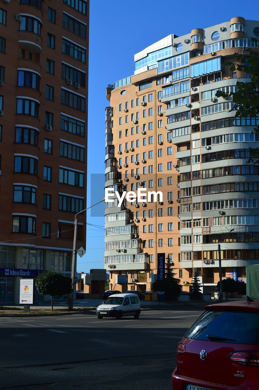 TRAFFIC ON ROAD BY BUILDINGS AGAINST SKY