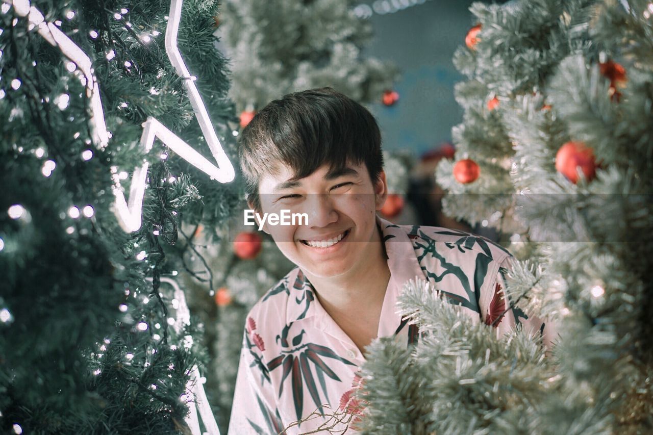 Portrait of smiling man amidst christmas tree