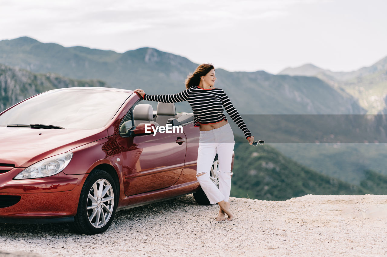 WOMAN WITH UMBRELLA STANDING ON MOUNTAIN ROAD