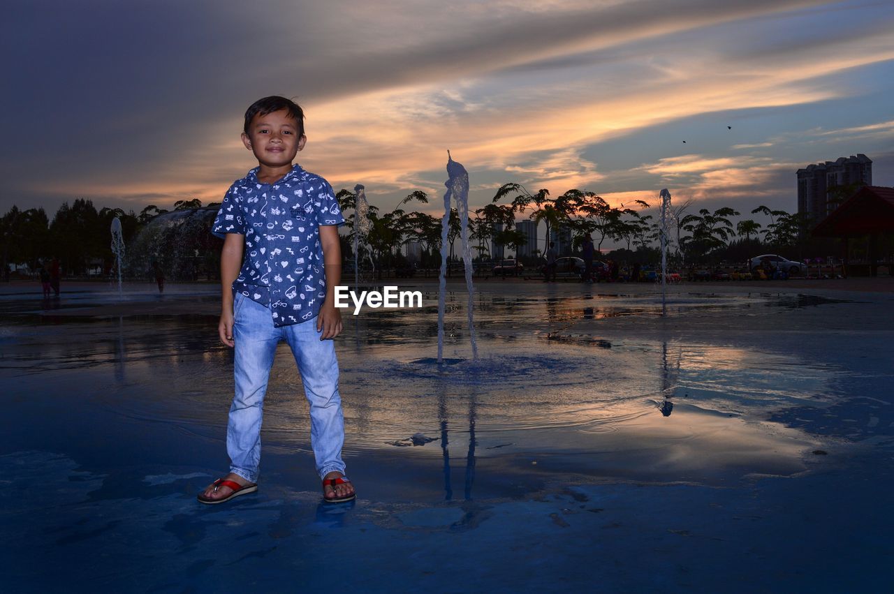 Boy standing by fountain at sunset