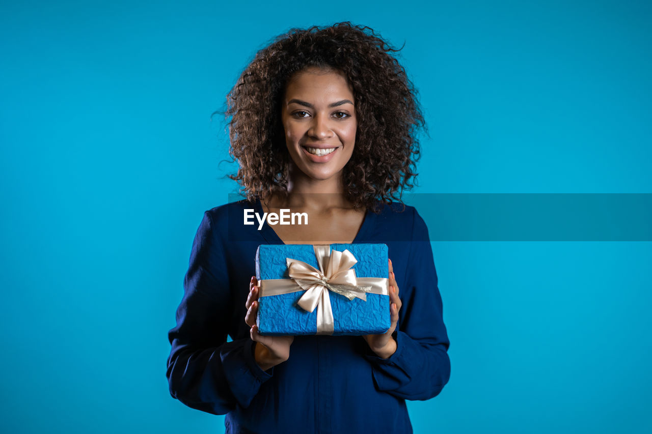 PORTRAIT OF A SMILING YOUNG WOMAN HOLDING BLUE BACKGROUND